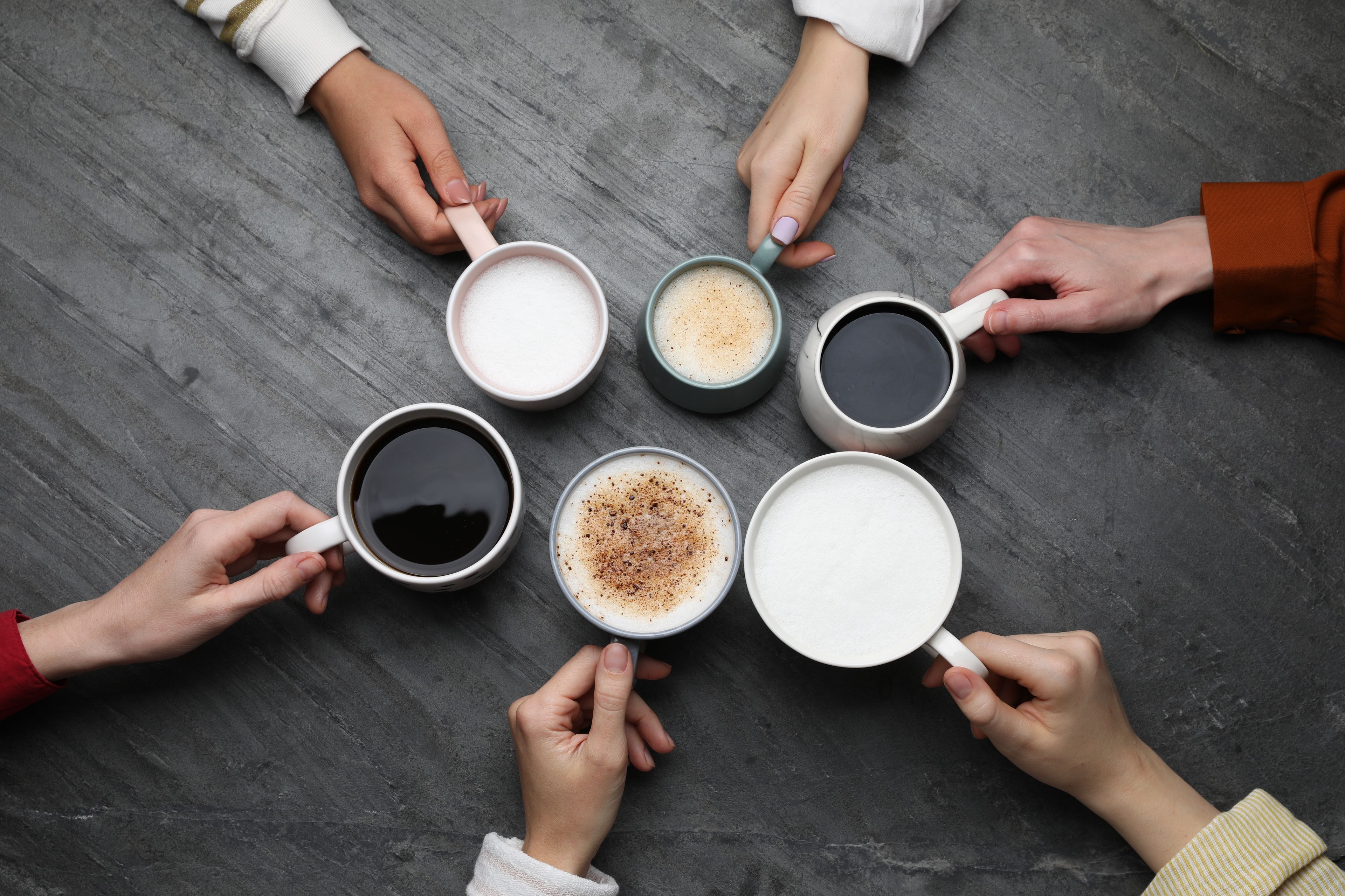 six people holding coffee cups in a circle